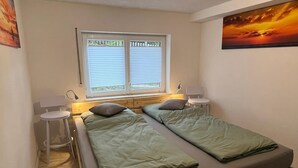 A small, cozy room with two single beds, a window with blinds, a small table, and a chair. - FeWo meisteroffice in Sackgässle, ground floor apartment, terrace, kitchen, near Ulm (Dornstadt)