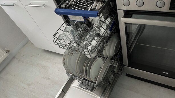 A dishwasher with a blue handle and a dish rack filled with plates and glasses. - FeWo meisteroffice in Sackgässle, ground floor apartment, terrace, kitchen, near Ulm (Dornstadt)