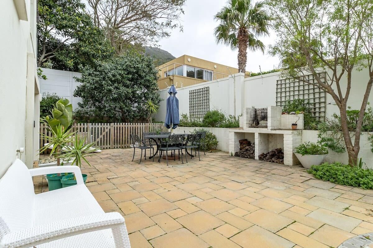 A patio with a table and chairs, a blue umbrella, and a white fence.