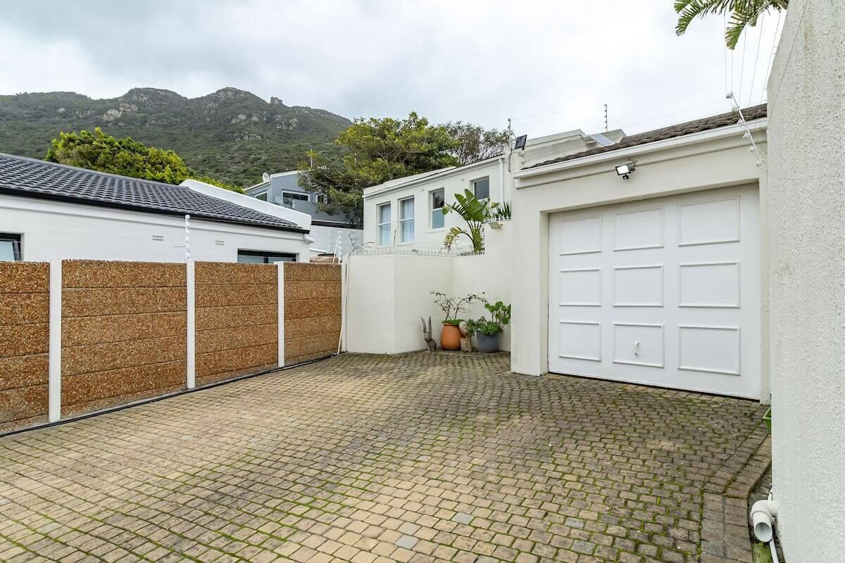 Un patio empedrado con una puerta de garaje blanca, una valla de madera y una planta en maceta.
