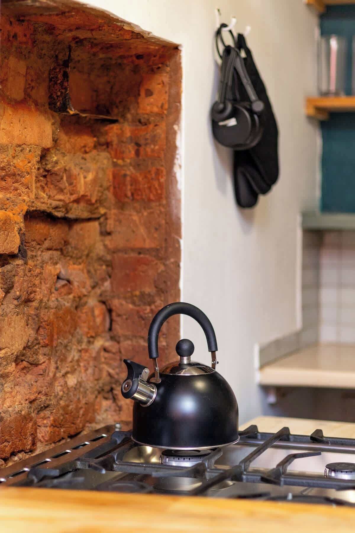 A kitchen with a gas stove, a kettle, and a brick wall.
