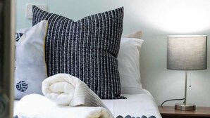 A neatly made bed with white and black bedding, a lamp on a bedside table, and a view of a room with a door. - Funky Pet Friendly, 2-bedroom Escape, Bo-kaap (Cape Town)