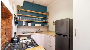 A kitchen with a gas stove, a black refrigerator, and wooden shelves above the counter. - Funky Pet Friendly, 2-bedroom Escape, Bo-kaap (Cape Town)