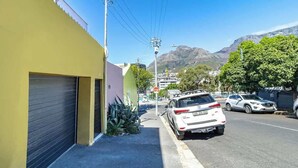 A street with parked cars, a yellow building, and mountains in the background. - Funky Pet Friendly, 2-bedroom Escape, Bo-kaap (Cape Town)
