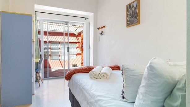 A bedroom with a bed, a window, and a view of an outdoor area. - Funky Pet Friendly, 2-bedroom Escape, Bo-kaap (Cape Town)