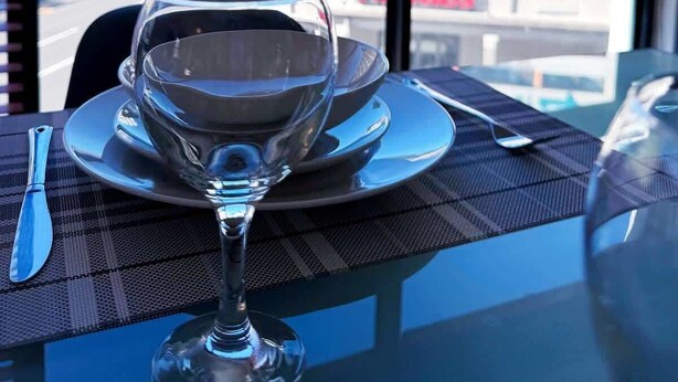 A table with a wine glass, plate, and cutlery set. A window reveals a cityscape with buildings and a mountain. - Spacious 1 Bedroom Apartment, Atlantica, Seapoint (Cape Town)