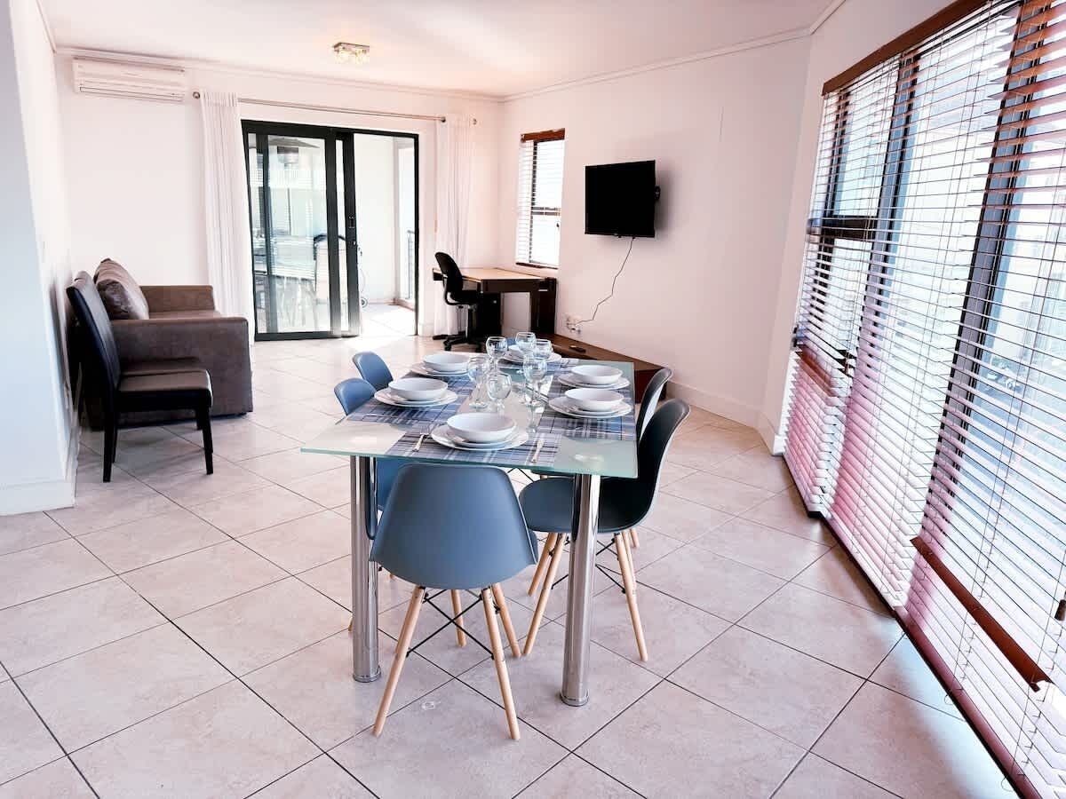 Comedor con una mesa de vidrio dispuesta para cuatro personas, rodeado de sillas.