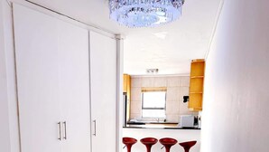A modern kitchen with white cabinets, a central island, and red bar stools. - Spacious 1 Bedroom Apartment, Atlantica, Seapoint (Cape Town)