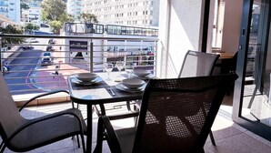 A balcony with a table set for dining, chairs, and a view of a street and buildings. - Spacious 1 Bedroom Apartment, Atlantica, Seapoint (Cape Town)