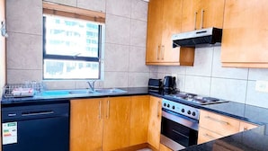 A modern kitchen with wooden cabinets, a built-in dishwasher, a stove, and a window with a view of buildings. - Spacious 1 Bedroom Apartment, Atlantica, Seapoint (Cape Town)