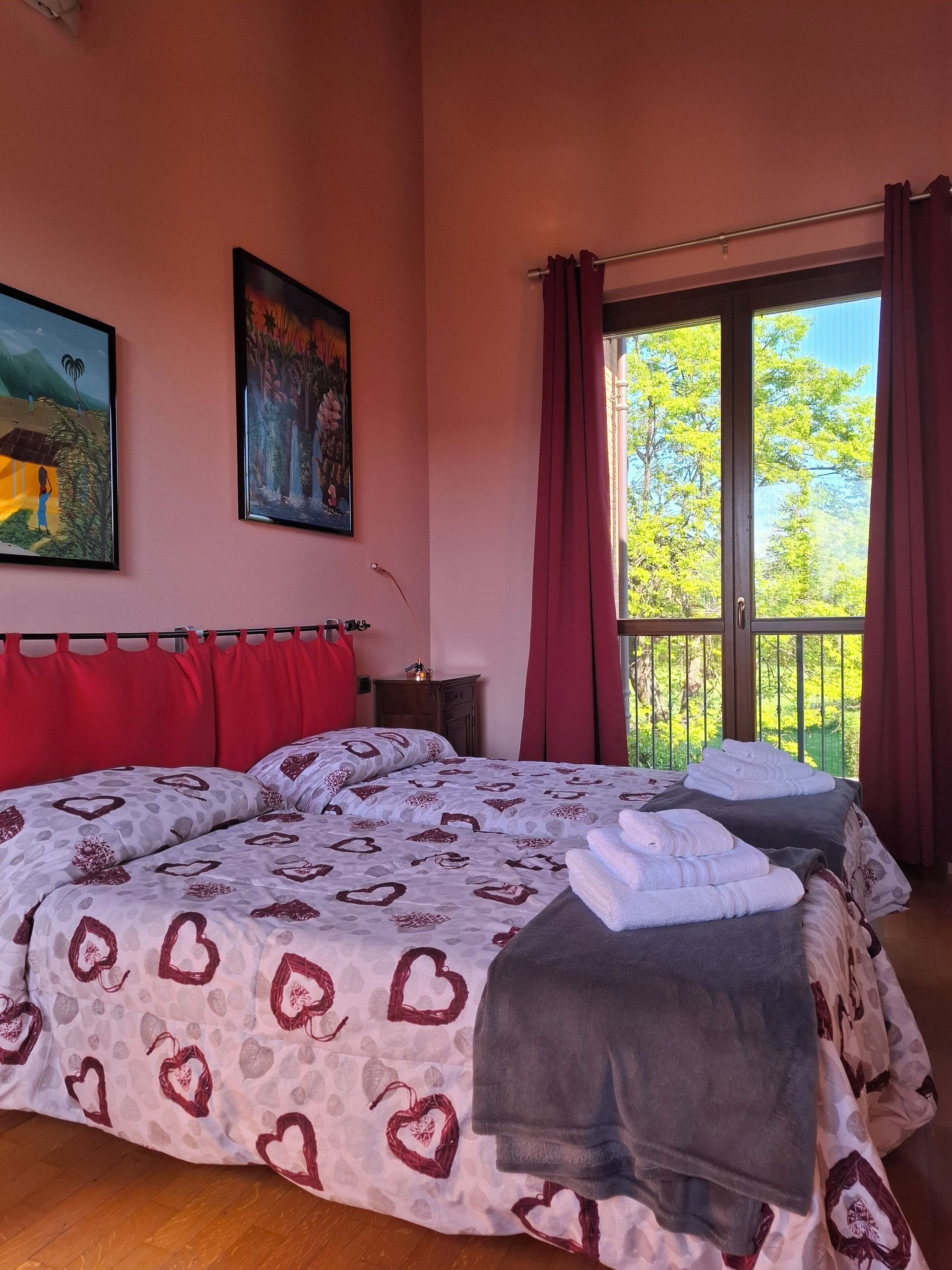 Une chambre avec un grand lit, des rideaux rouges et deux tableaux accrochés au mur.