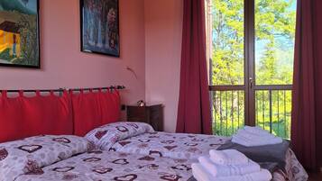 Une chambre avec un grand lit, des rideaux rouges et deux tableaux accrochés au mur.