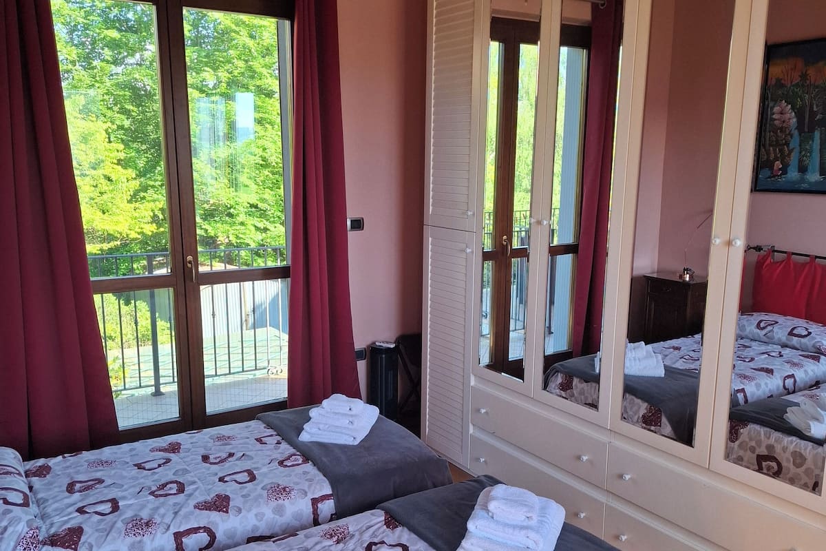 A bedroom with two beds, a large wardrobe with mirrors, and a balcony with red curtains.