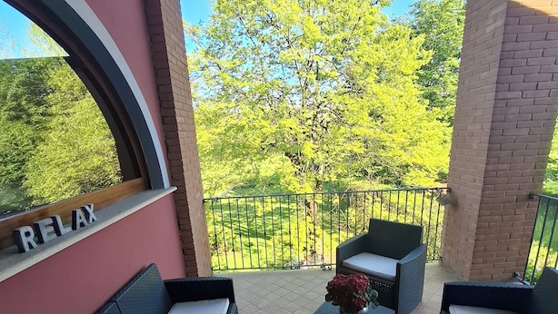 A balcony with wicker furniture, a view of trees, and a brick wall. - B&B Rubino (Cervasca)