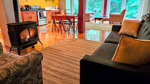 Una sala de estar acogedora con chimenea, zona de comedor y amplias ventanas que ofrecen vistas a la vegetación.