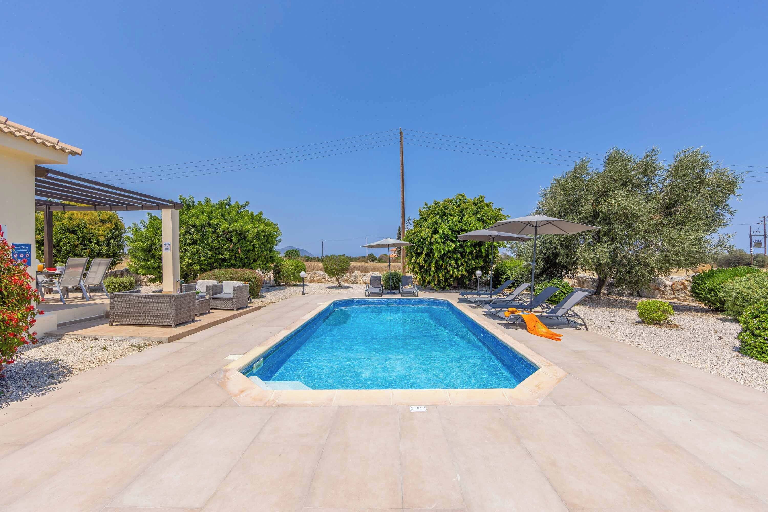 A rectangular swimming pool with a tiled deck, surrounded by lounge chairs and umbrellas.