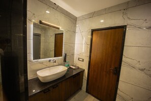 A modern bathroom with a marble wall, a large sink, and a wooden door. - Hotel Shankar Palace Beawar (Beawar)