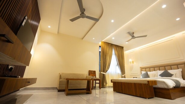 A modern hotel room with a large bed, a sofa, a desk, and two ceiling fans. - Hotel Shankar Palace Beawar (Beawar)