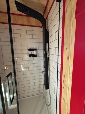 A shower area with white tiled walls, a black showerhead, and a wooden door frame.