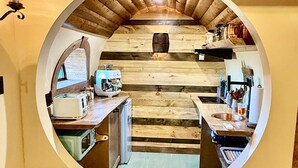A circular view of a rustic kitchen with wooden beams, a central barrel, and basic amenities. - Terra Experience (Shippagan)