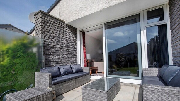 An outdoor patio area with wicker furniture, a stone wall, and a sliding glass door leading to a covered space. - Beautiful spacious house Airport (Edinburgh)