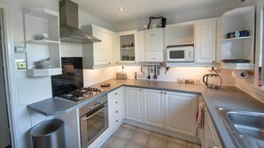 A modern kitchen with white cabinetry, a gas stove, an oven, a microwave, and a sink. - Beautiful spacious house Airport (Edinburgh)