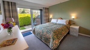 A bedroom with a large bed, a bedside table with a lamp, a nightstand, and a view of the outdoors through a sliding door. - Beautiful spacious house Airport (Edinburgh)