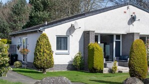 A single-story house with a white exterior, satellite dish, and a small porch with outdoor furniture. - Beautiful spacious house Airport (Edinburgh)