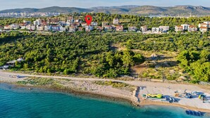 Vista aérea de un pueblo costero con edificios residenciales, una playa y montañas al fondo.