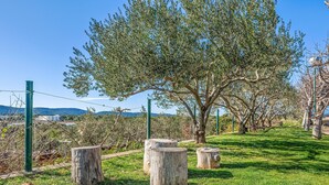 Un parque con un árbol grande, troncos de madera y una valla metálica.