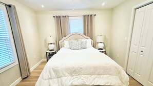 Une chambre avec un grand lit, deux tables de chevet avec des lampes, un ventilateur de plafond et une armoire.