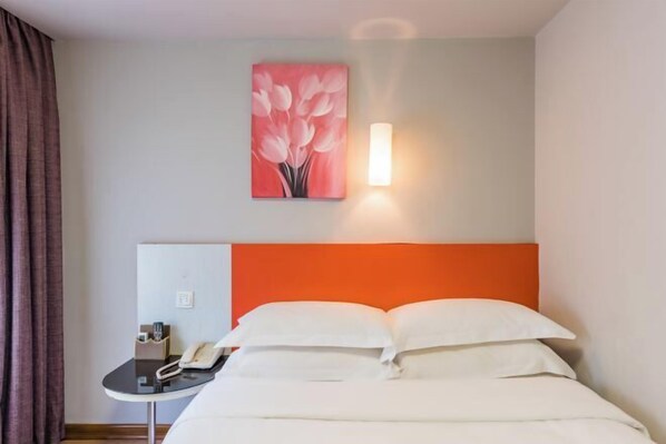 A hotel room with a bed, a bedside table with a phone, a painting on the wall, and a light fixture.