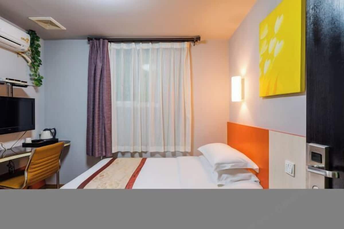 Ein Hotelzimmer mit Bett, Schreibtisch mit Stuhl, Fernseher und einem Fenster mit Vorhängen.