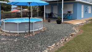 Una casa azul de dos pisos con un porche cubierto, una piscina y un garaje.