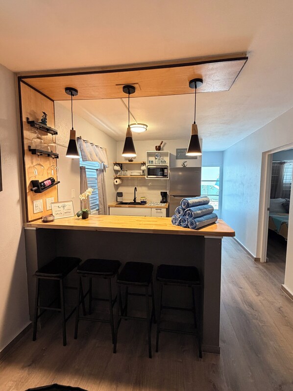 Uma cozinha compacta com bancada de madeira, luminárias pendentes, micro-ondas e pia.