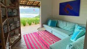 Ein Zimmer mit einer gemusterten Couch, einem Korbbuschregal und Blick ins Freie.