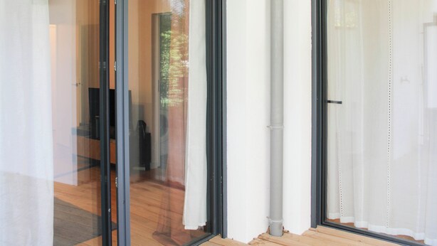 Un interior moderno con puertas de cristal que dan a una habitación con suelo de madera y una silla a la vista.