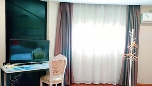 A room with a flat-screen TV on a glass table, a chair, a coat rack, and a large window with curtains. - Junyi Hotel (Shanghai Chongming District Xue Gong Road ) (Shanghai)