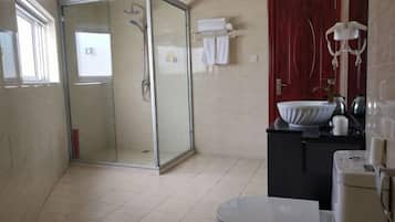 Een badkamer met een douche met glazen wand, een wastafel, een toilet en een rode deur.