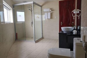 A bathroom with a glass-enclosed shower, a sink, a toilet, and a red door. - Junyi Hotel (Shanghai Chongming District Xue Gong Road ) (Shanghai)
