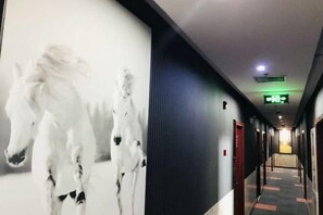 Un couloir d’hôtel avec un tableau représentant un cheval accroché au mur, une moquette à motifs et un panneau de signalisation verte indiquant la sortie.