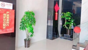 A modern lobby with a clean, polished floor, two potted plants, a red decorative hanging, and a sign with Chinese characters. - Junyi Hotel (Shanghai Chongming District Xue Gong Road ) (Shanghai)