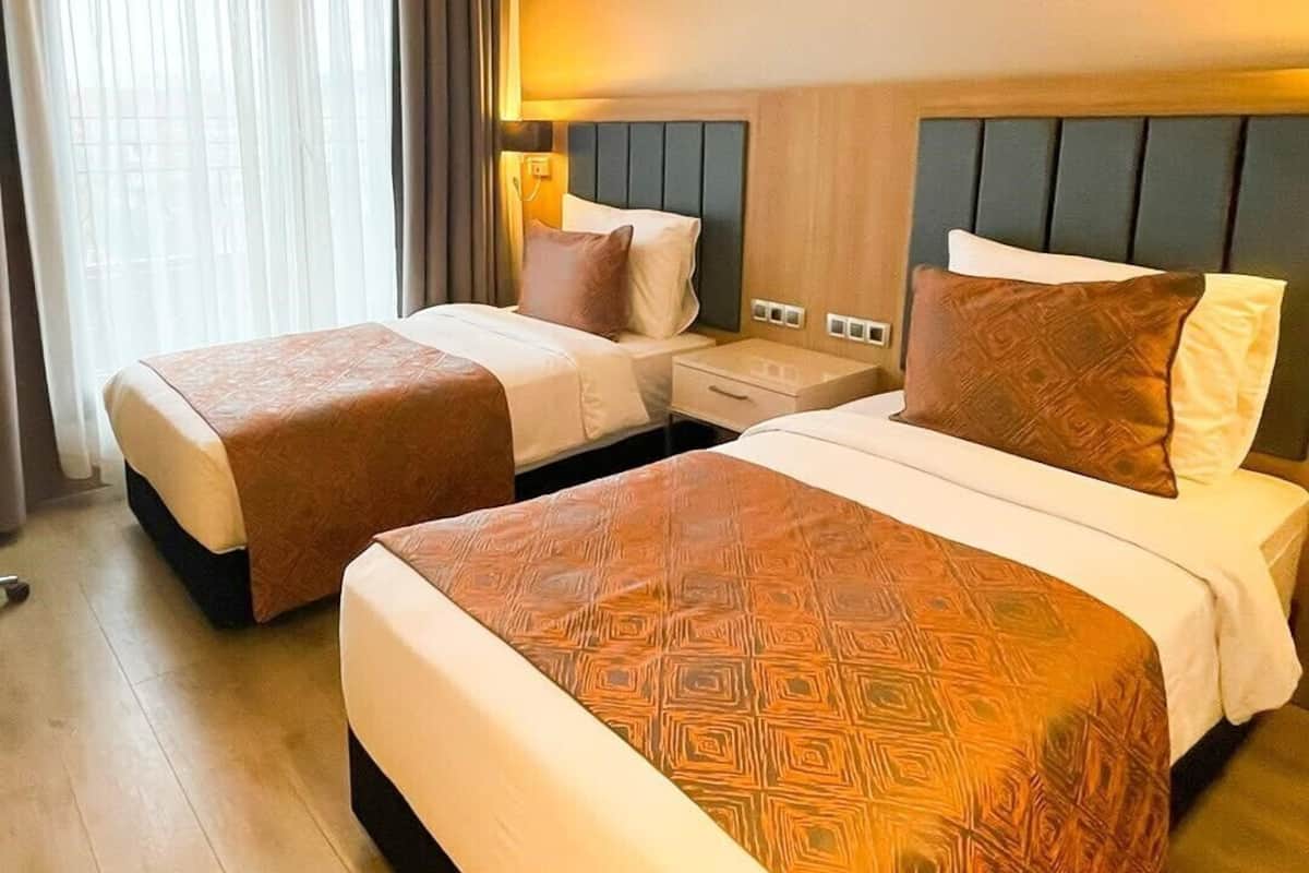 A hotel room with two beds, a large window with curtains, and a wooden headboard.