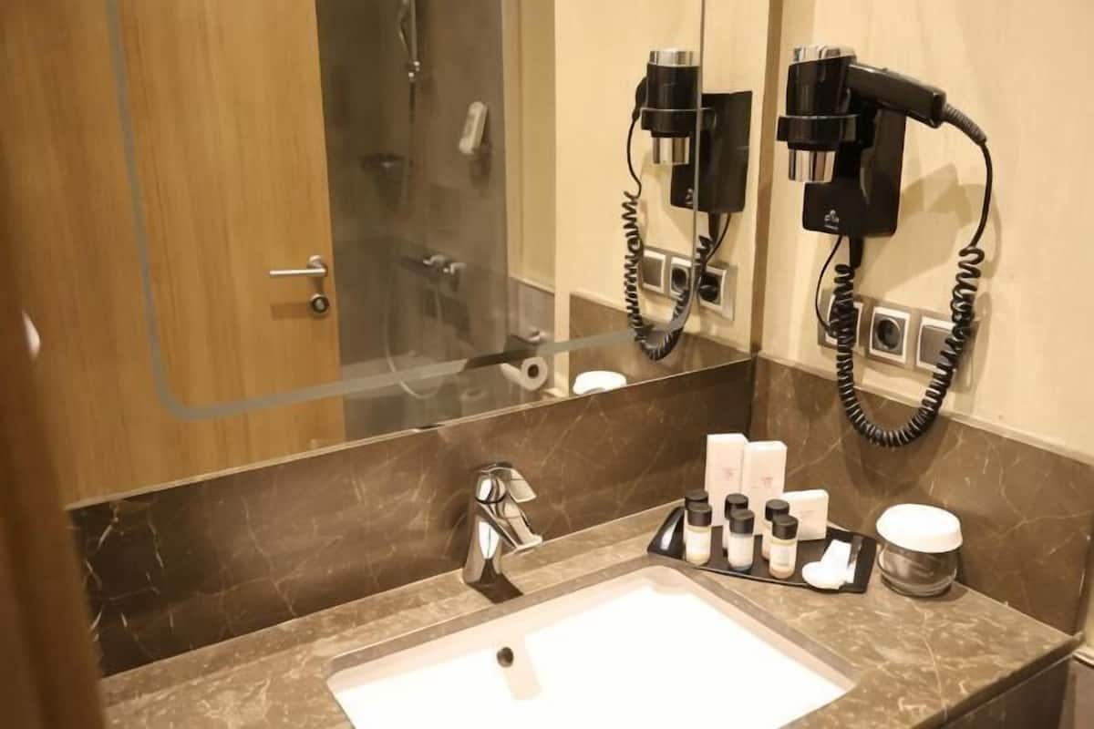 A bathroom with a sink, mirror, hairdryer, and toiletries.