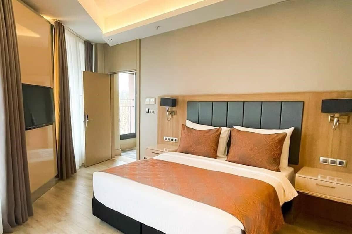 A modern hotel room with a large bed, a flat-screen TV, and a sliding door to the balcony.