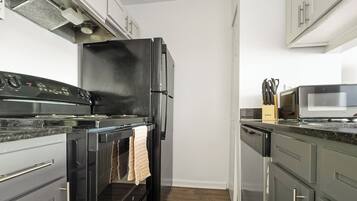Una cocina con estufa, horno y refrigerador negros, armarios de acero inoxidable y un microondas sobre la encimera.