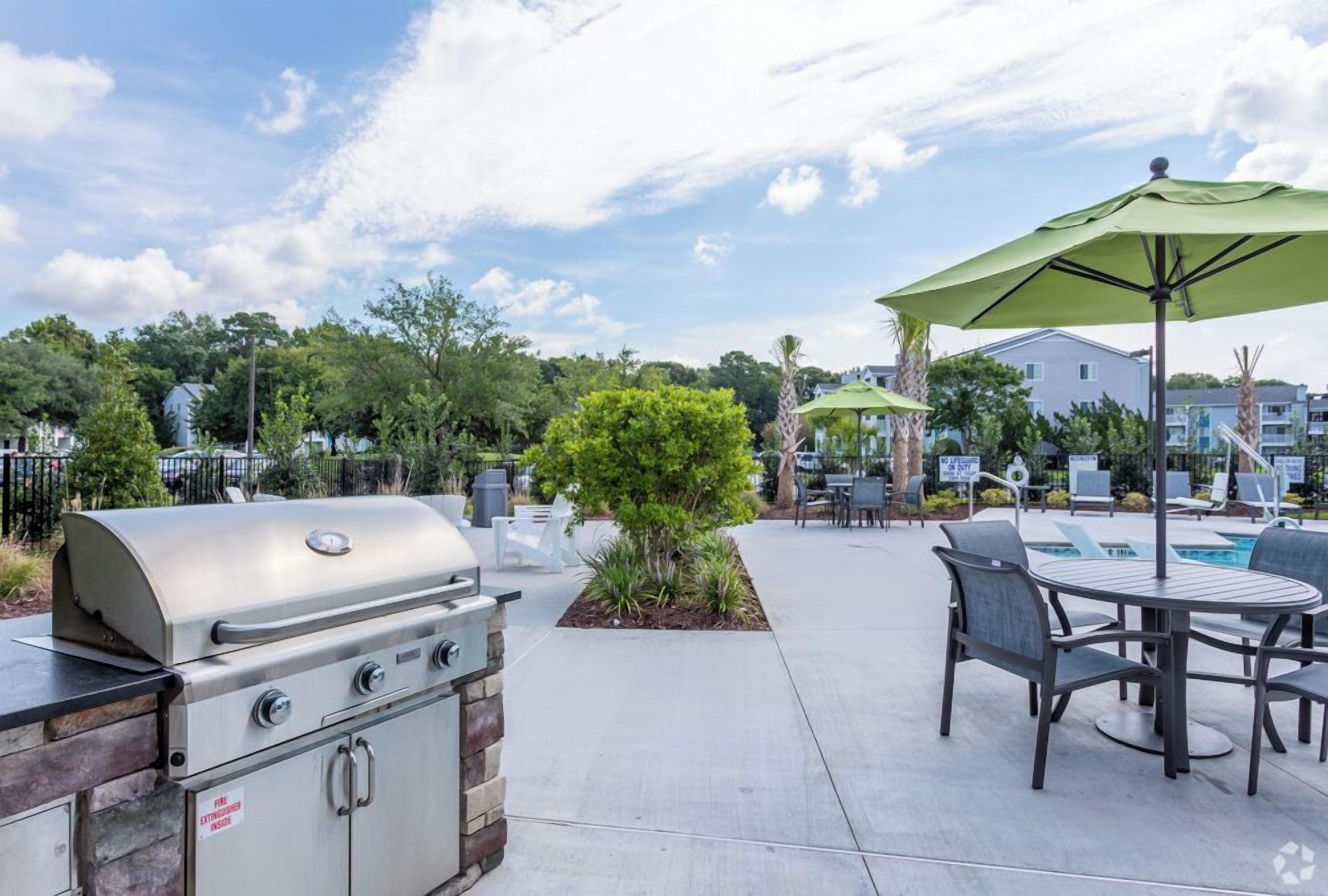 An outdoor patio area with a barbecue grill, a pool table, and outdoor seating with umbrellas.