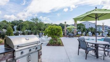 An outdoor patio area with a barbecue grill, a pool table, and outdoor seating with umbrellas.