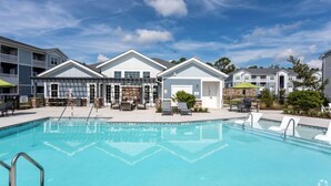 A swimming pool with lounge chairs and a covered seating area, surrounded by multi-story buildings with balconies. - Landing Myrtle Beach (Socastee)