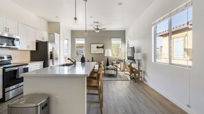 A modern kitchen with a central island, stainless steel appliances, and a dining area with a TV and seating. - Landing Apartments Oro Valley (Oro Valley)